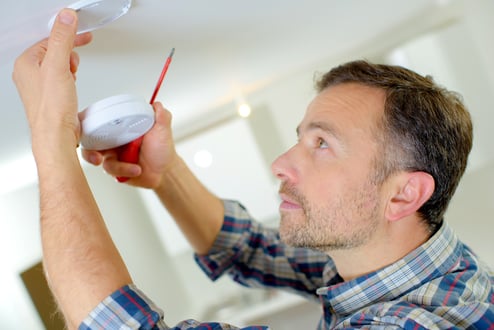 man installs a smoke detector in home