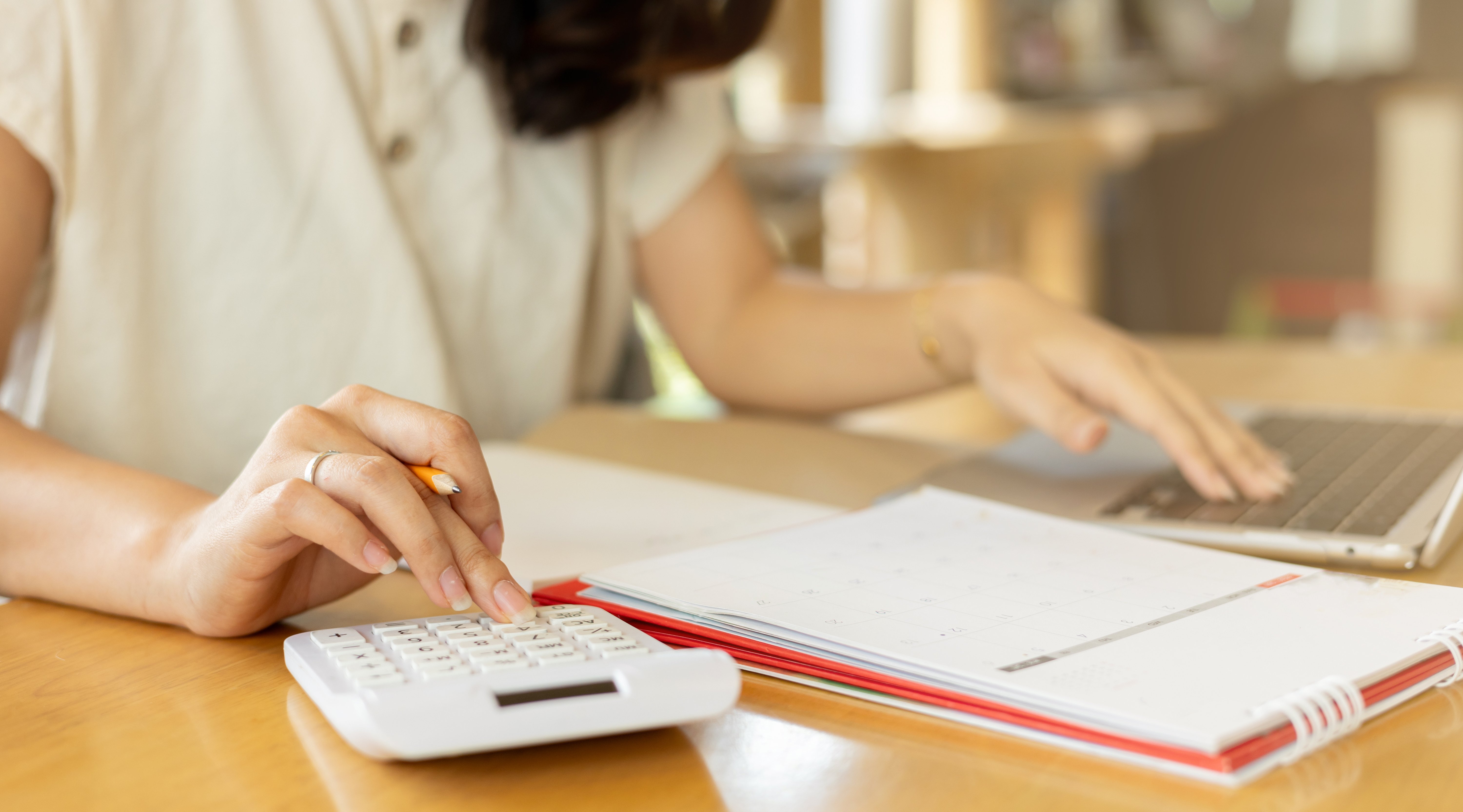 Close up young woman using a calculator with an open notebook and laptop