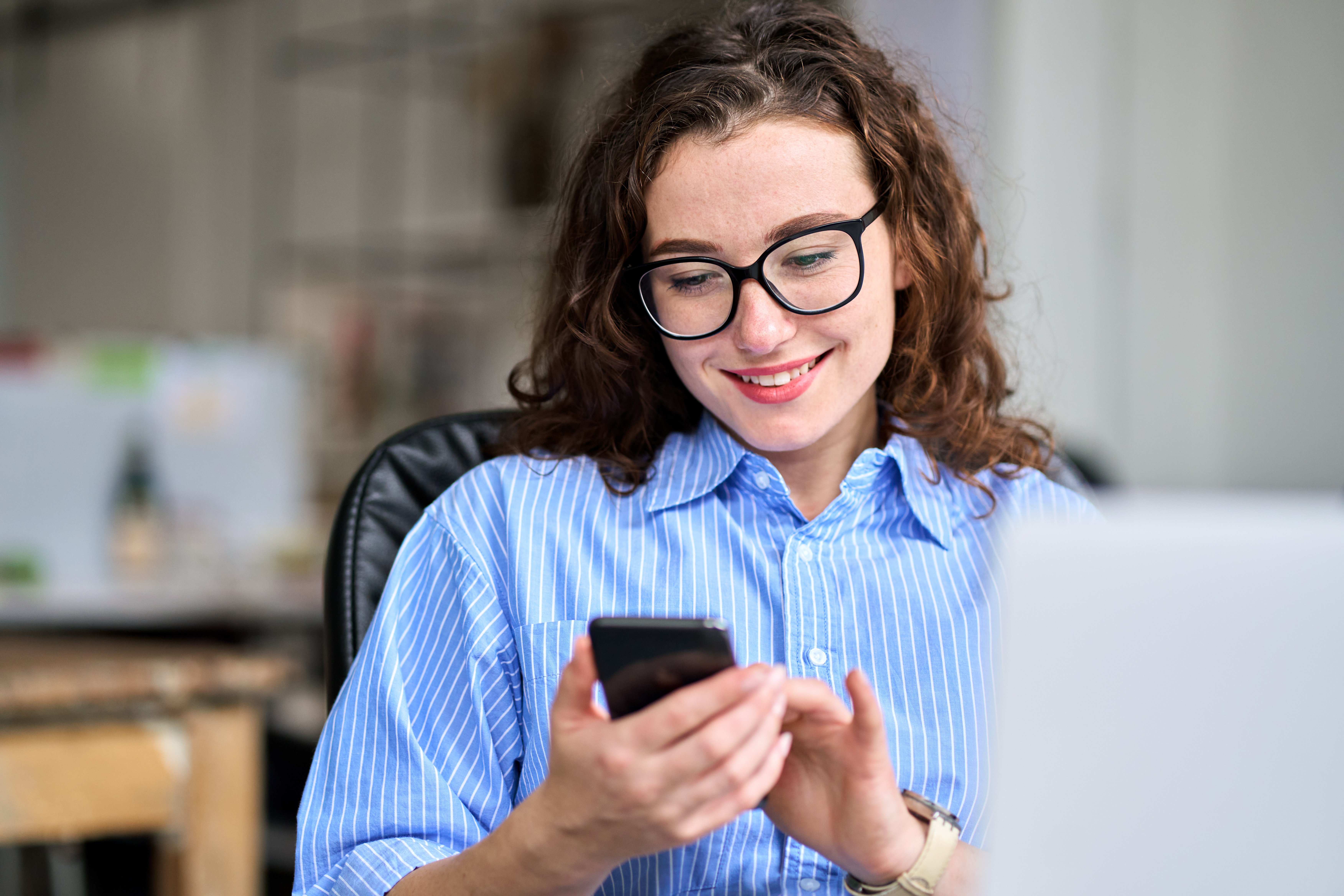Professional female working in office using a mobile cell phone sitting at desk and smiling.