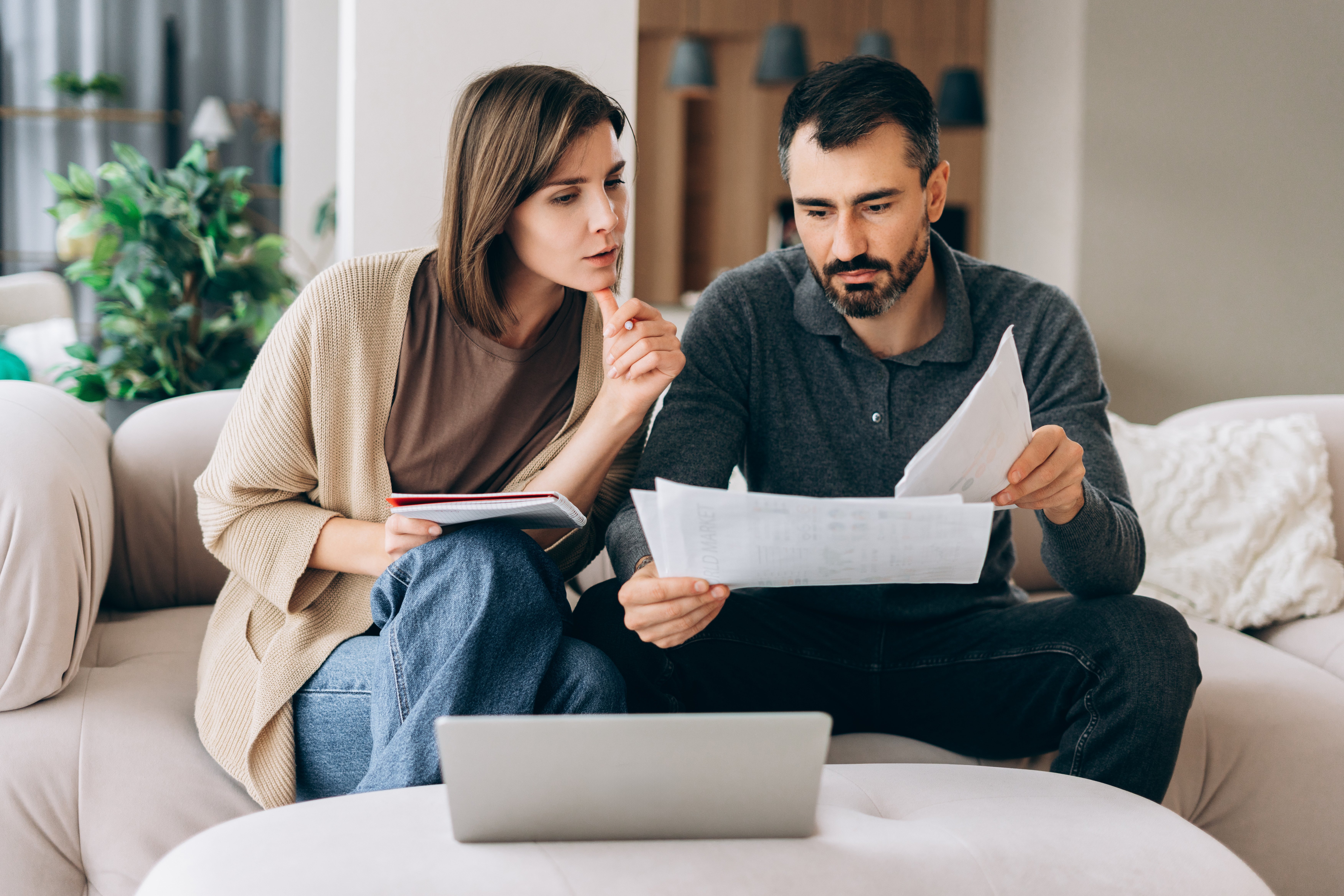 Man and women sitting on couch looking at paperwork and computer