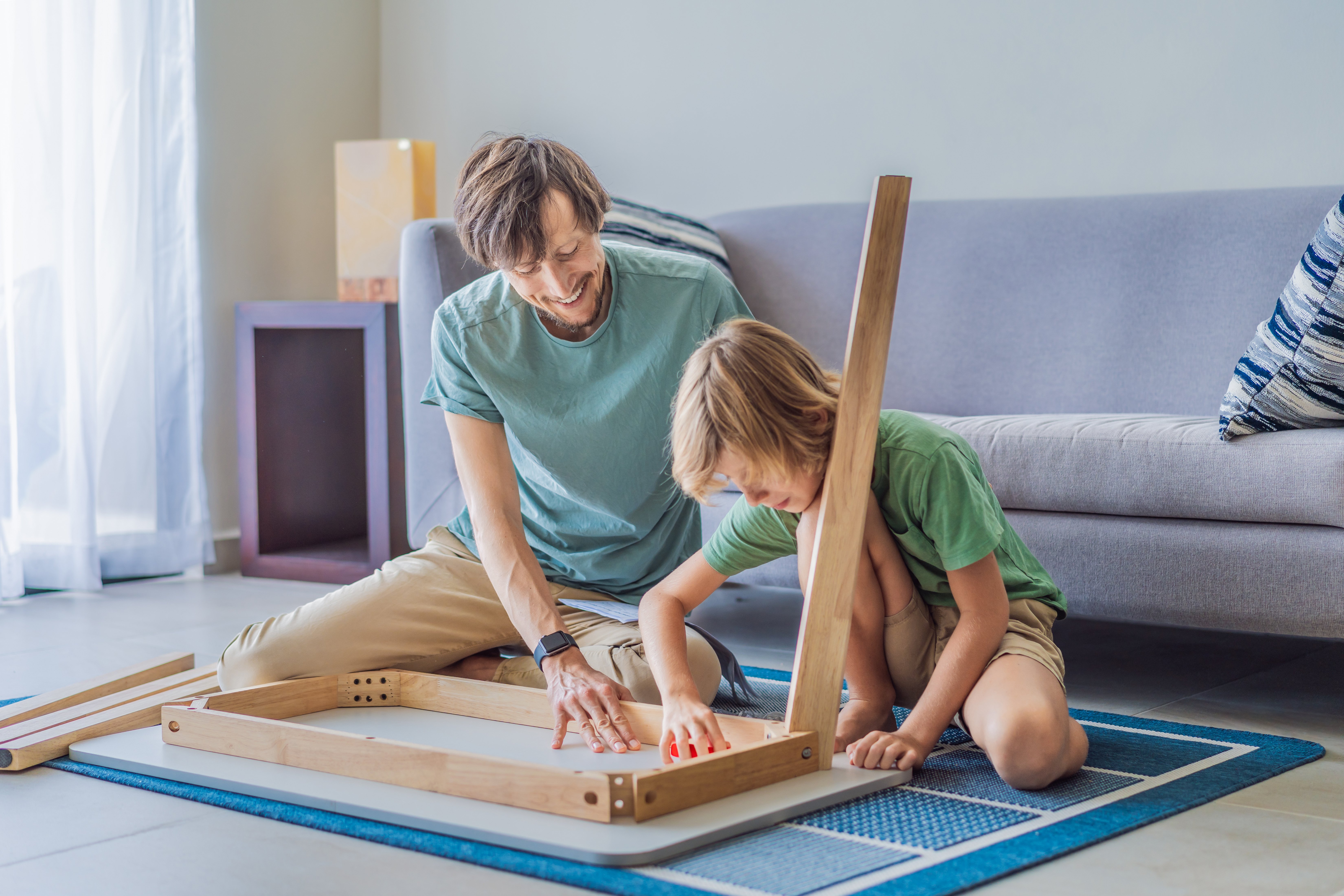 Father and his son assembling a table together in the living room at home.