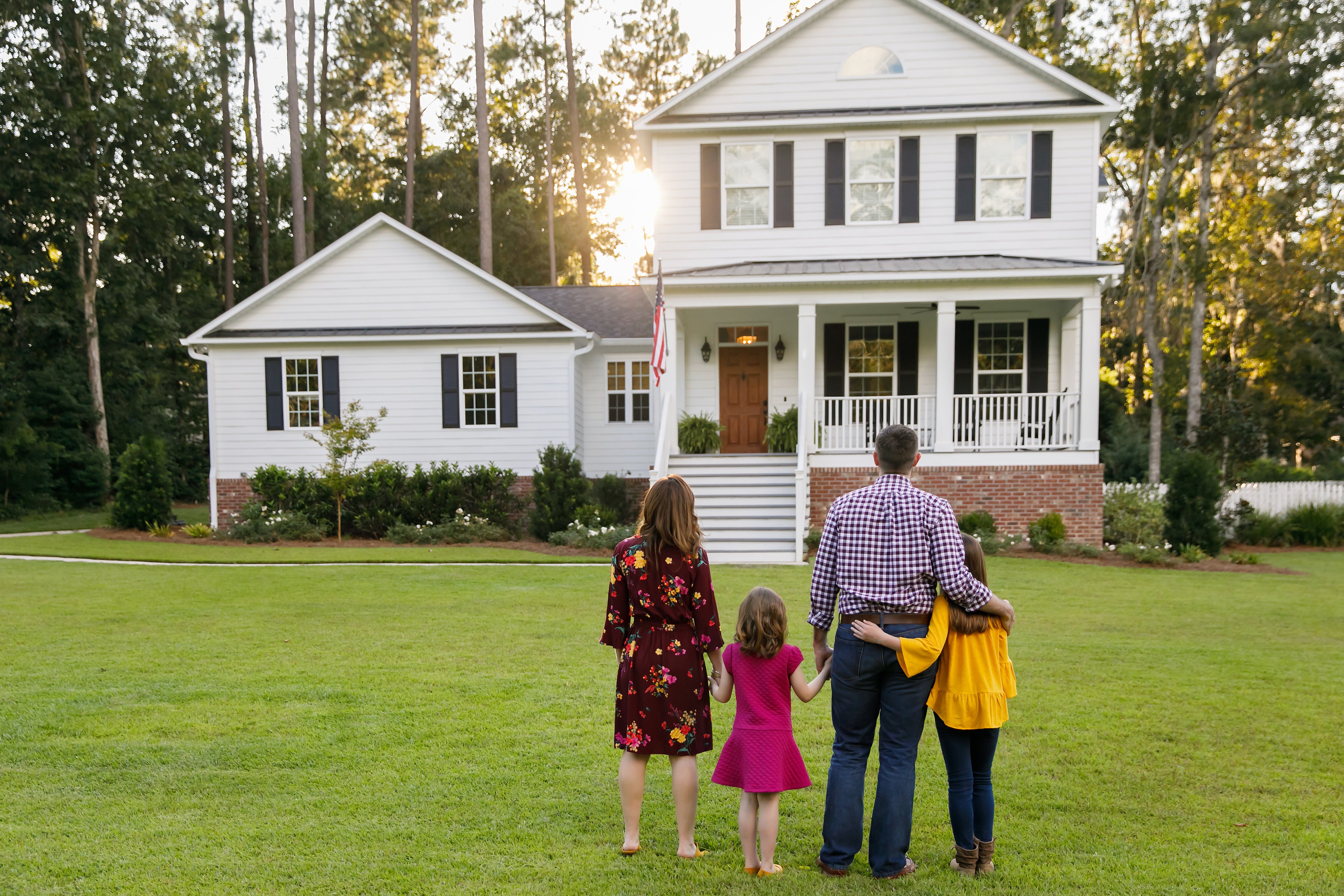 Family of Four With Daughters Looking at Their New Construction White Farmhouse Home