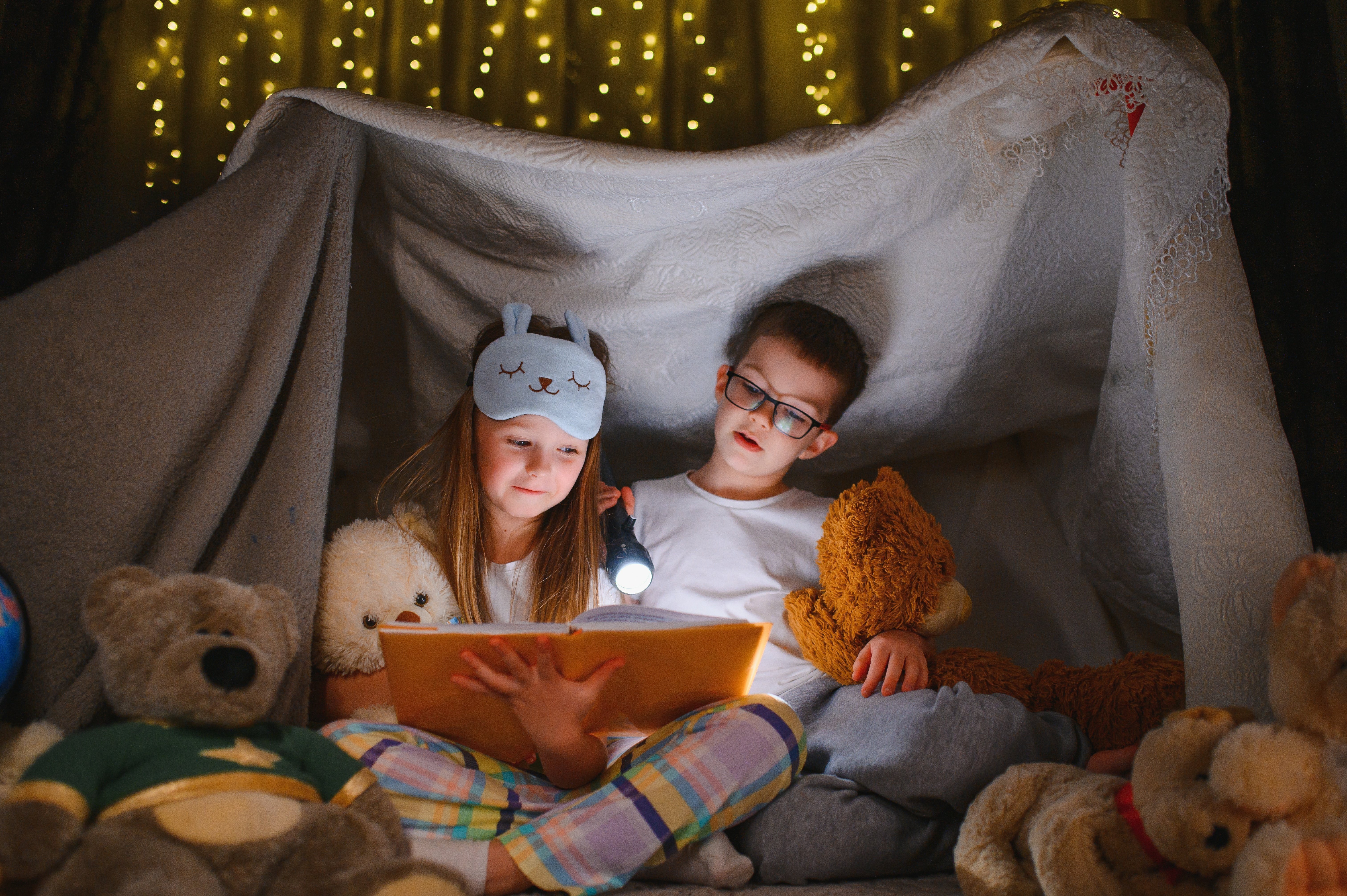 Children reading bedtime story at home in a blanket fort.