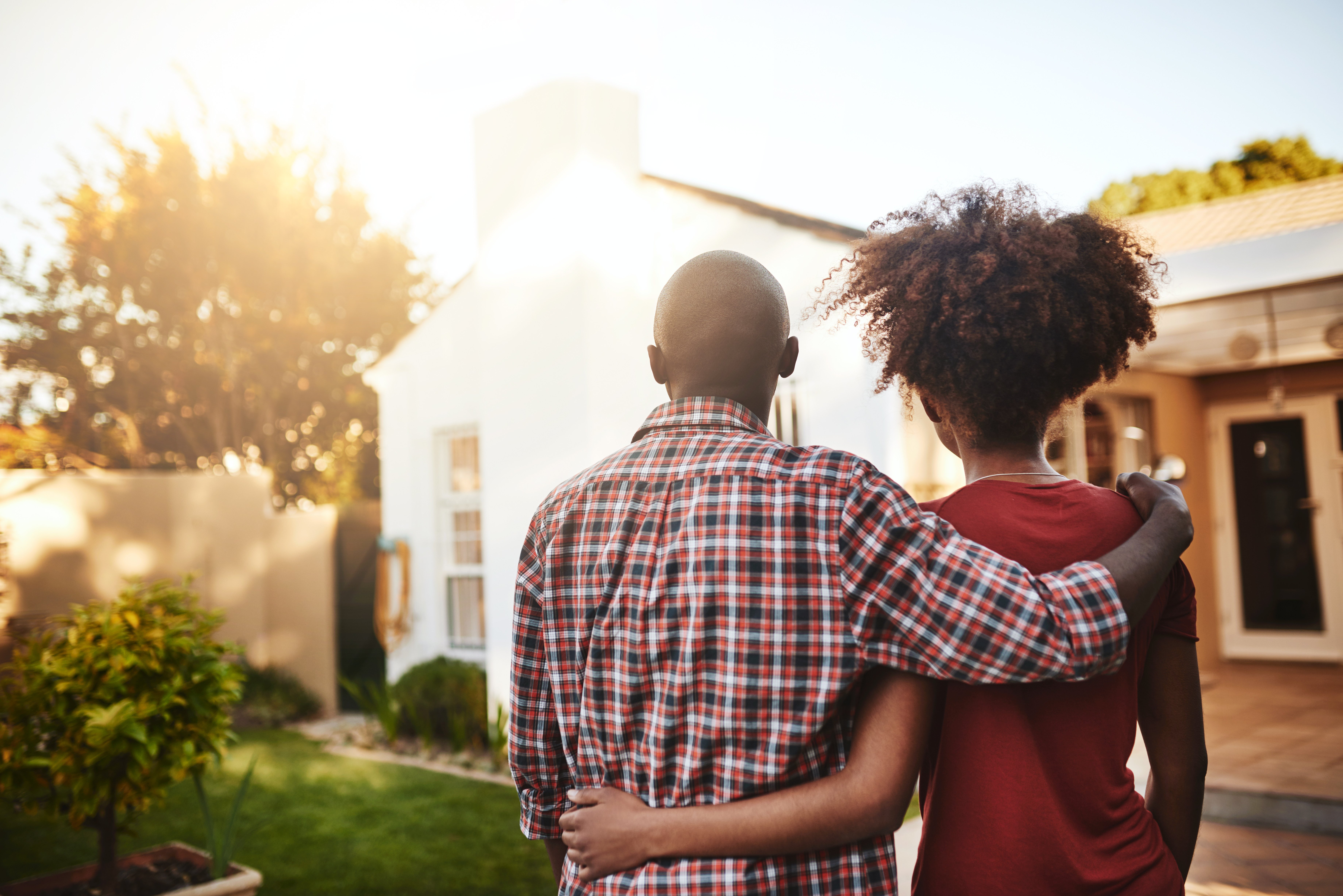 Couple with their backs toward the audience, looking at a house with an arm around each other.