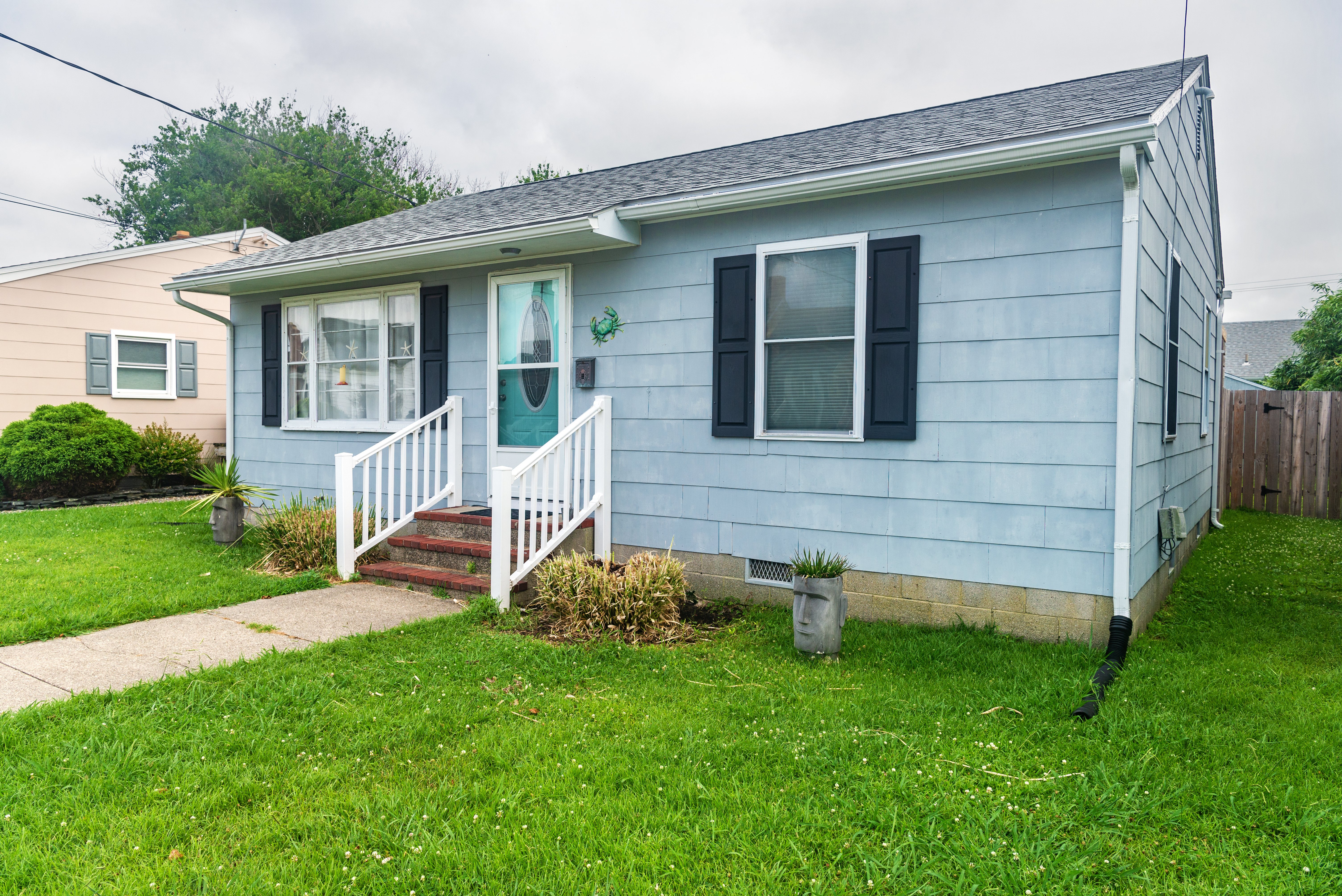 Exterior view of one-story home with a turquoise door, blue siding, and black shutters.