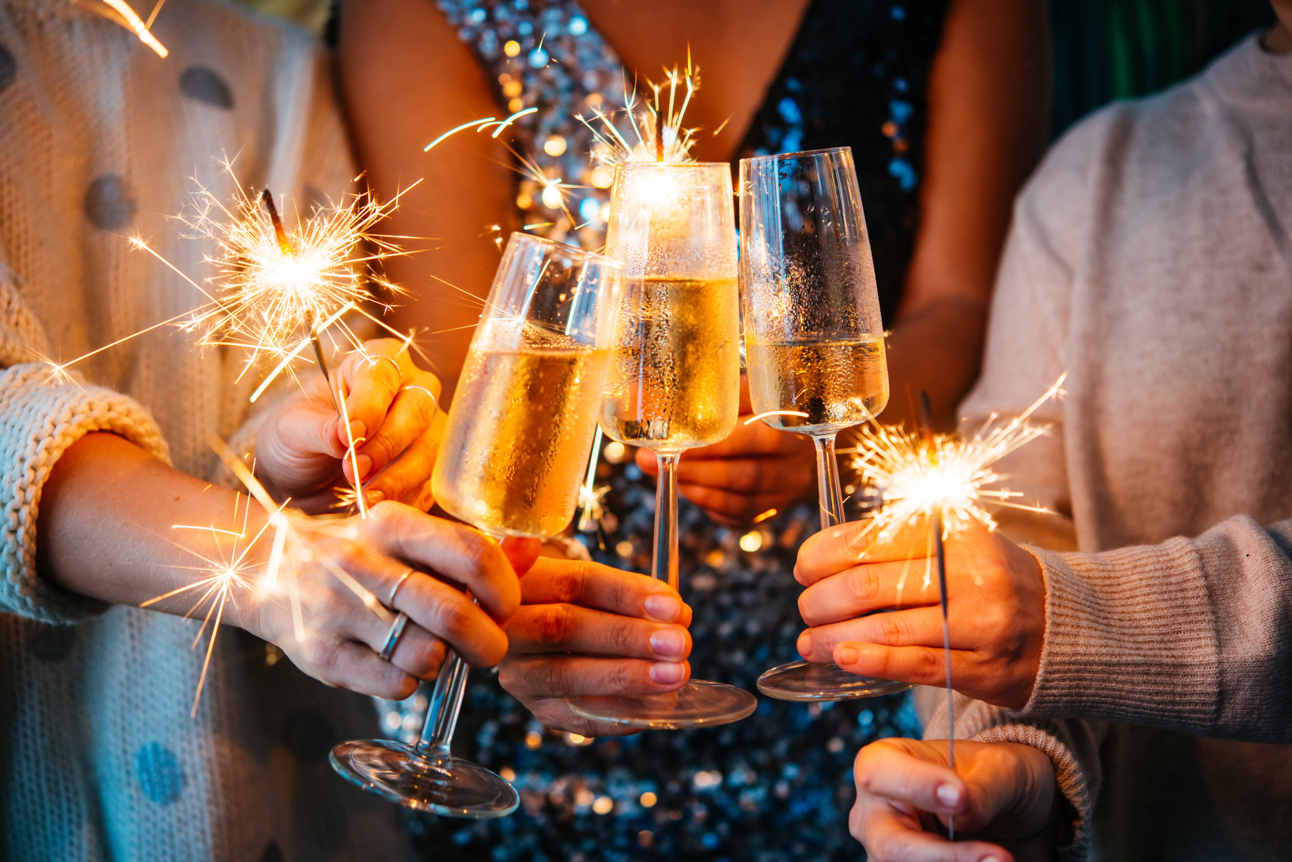 New Year celebration, three people holding glasses of champagne and sparklers.