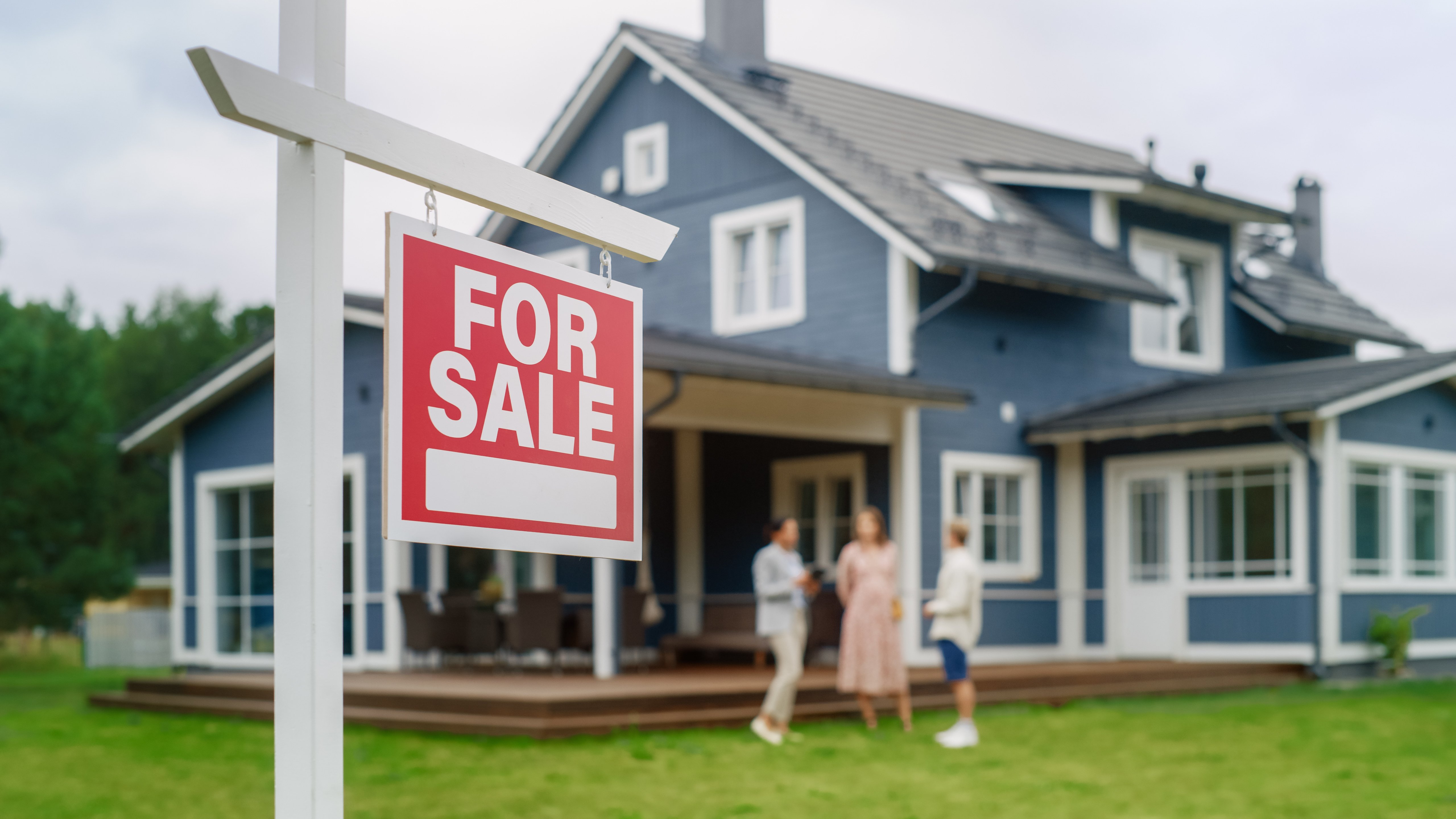 Young Couple Visiting a Potential New Home Property with Professional Real Estate Agent. Female Realtor Showing the Area to Future Homeowners. Focus on For Sale Sign