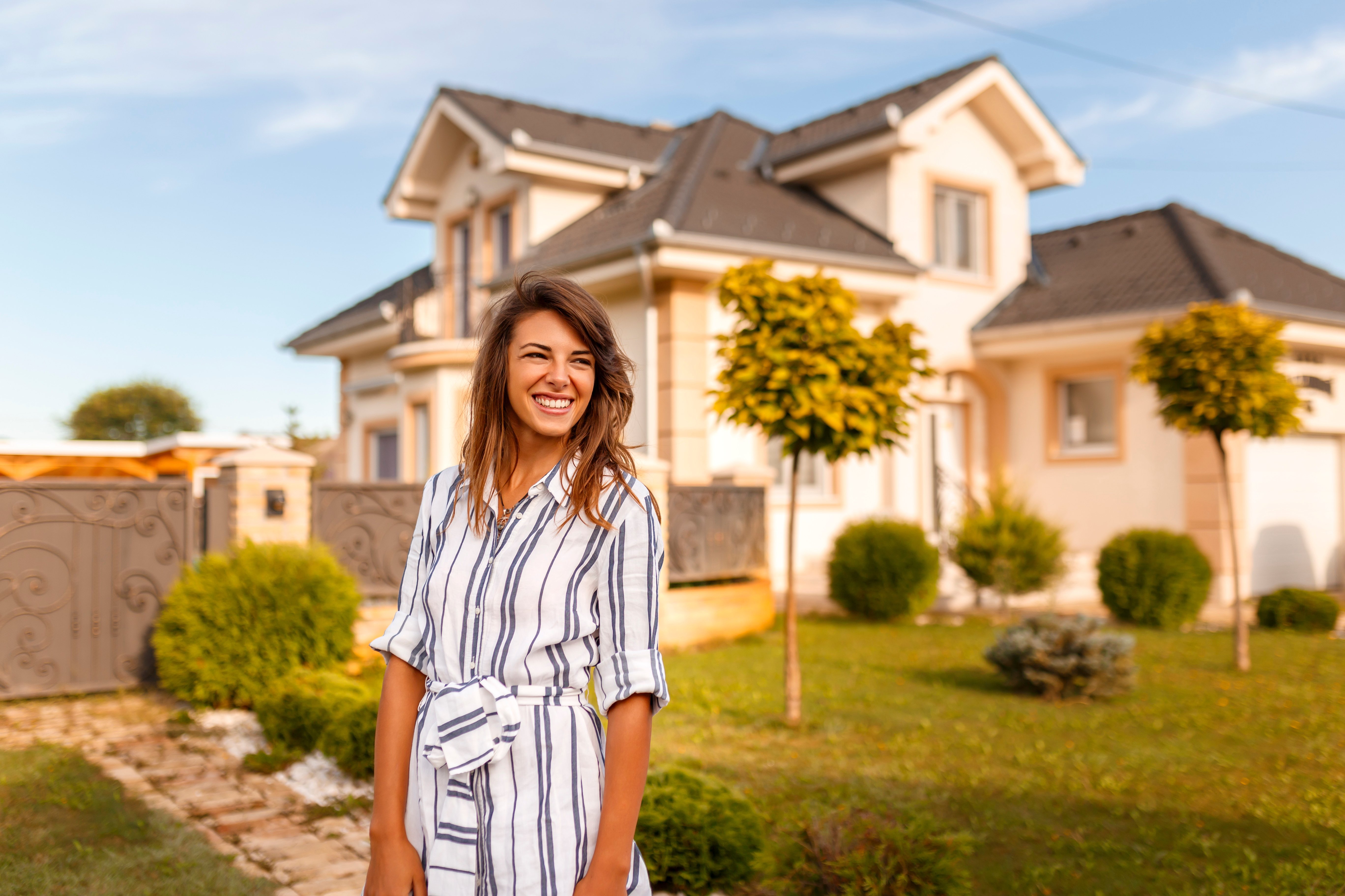 Woman standing in front of her new house, smiling outside with sun shining.