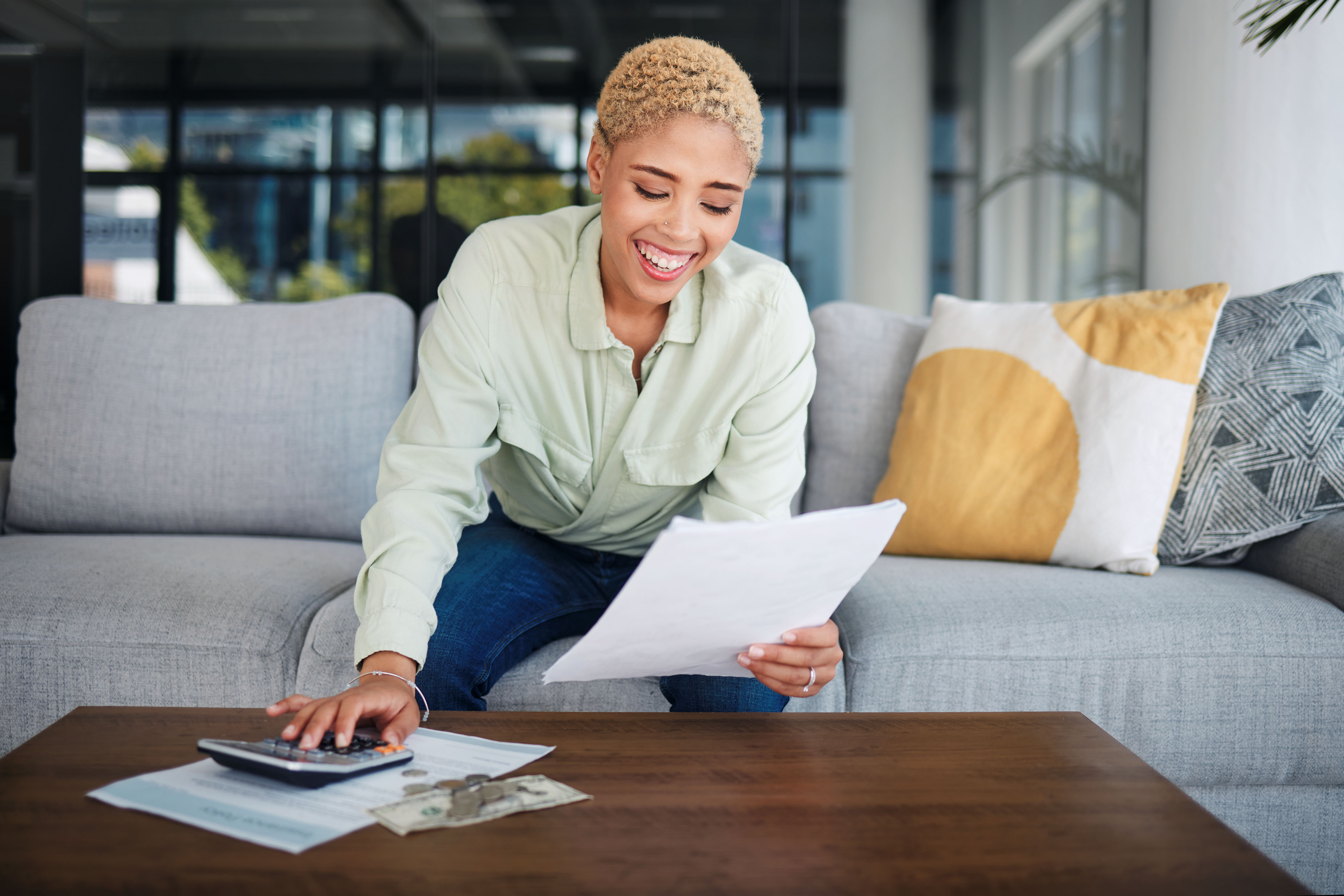 Woman smiling with calculator and budget on sofa for home financing and seeing how much she has saved.