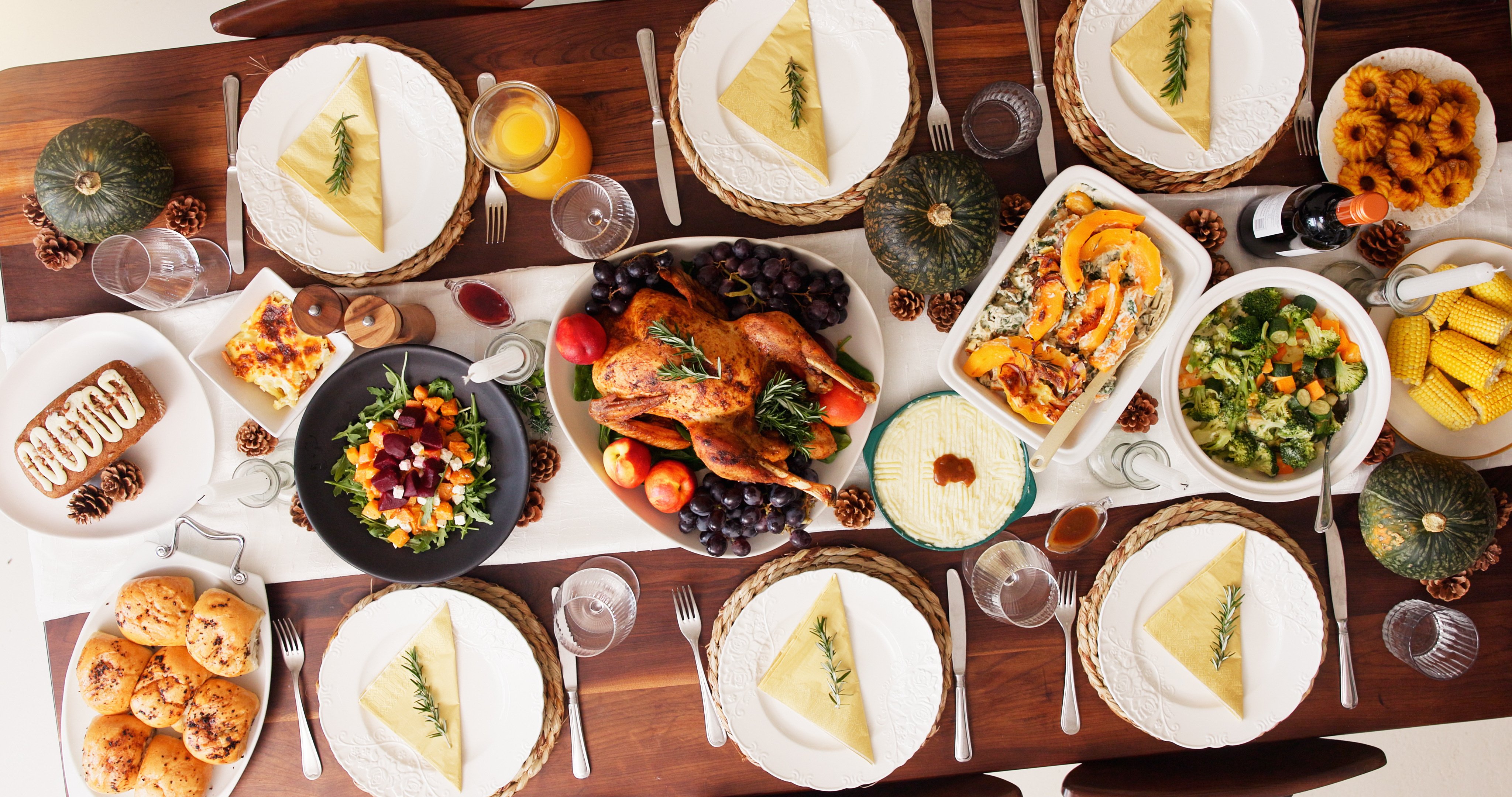 An overhead shot of a kitchen table set for Thanksgiving dinner and six place settings indicates that a meal is to begin soon.